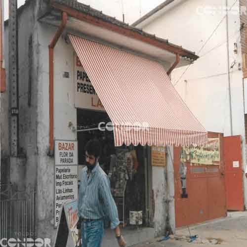 Homem passando embaixo de um toldo retrátil listrado instalado em um bazar