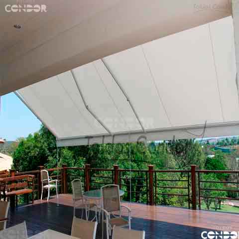 um grande toldo articulado basic aberto apoiado em hastes de seguranças enquanto protege um grande deck de madeira do sol