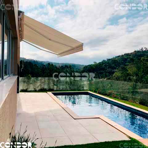um toldo articulado premium protegendo uma piscina na sacada com vista para a floresta
