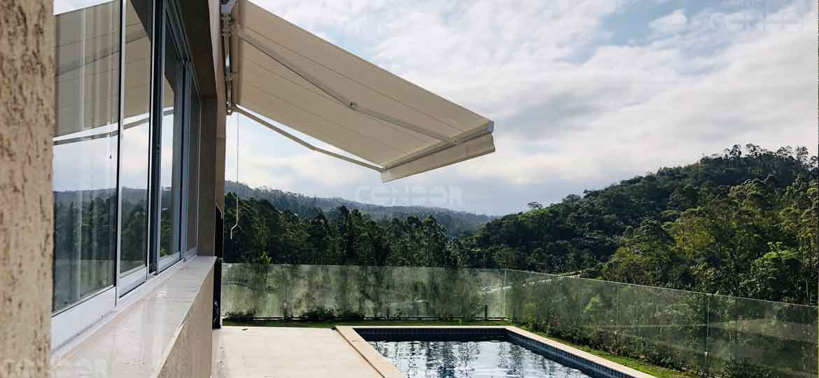 toldo articulado aberto de frente para uma piscina com vista para uma montanha repleta de arvores