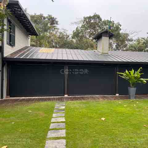 Toldos Premium Blocker instalados em uma residência com área externa gramada, oferecendo proteção contra intempéries e complementando o design moderno da fachada.