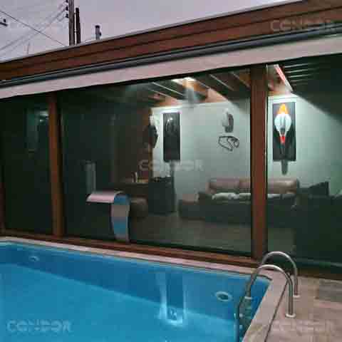 Toldo cortina Premium Blocker instalado em área com piscina, protegendo o espaço interno de uma sala com sofás e decoração moderna, combinando conforto e funcionalidade.