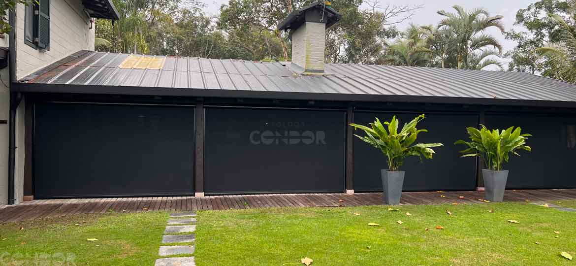 toldos verticais fechados escondendo o ambiente interno de uma casa cercada por vegetacao.