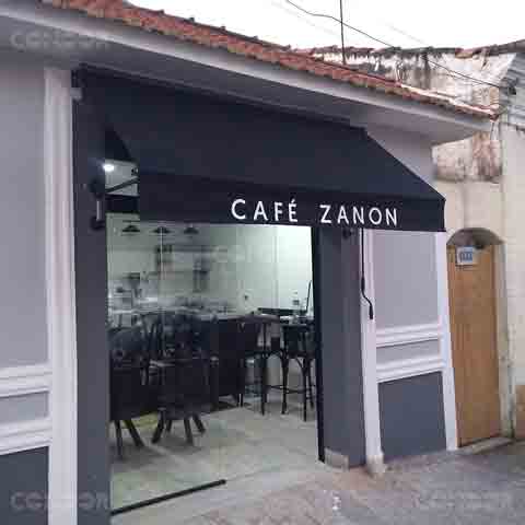Cafeteria moderna com toldo retrátil preto aberto e instalado na faixada contendo o logo tipo e nome do comércio.
