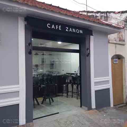 Cafeteria moderna com toldo retrátil preto recolhido e instalado na faixada contendo o logo tipo e nome do comércio.