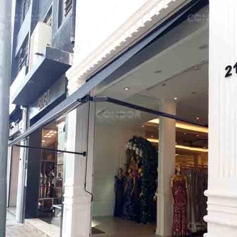 toldo retrátil premium aberto protegendo a entrada de uma loja de vestidos de luxo.